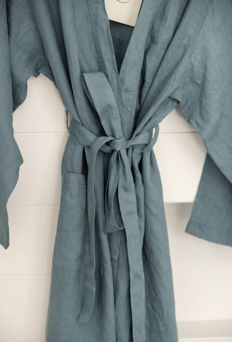 Linen Label Dust Denim Blue French Linen Bathrobe Kimono Robe hanging on a detailed cane hanger - looking luxurious and aesthetically pleasing in a sage green, perfect for ultimate comfort and relaxation. focusing on the waist tie and pockets 