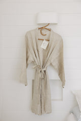 Linen Label Natural Oat Linen Bathrobe Kimono Robe hanging on a detailed cane hanger - looking luxurious, perfect for ultimate comfort and relaxation. Crafted with 100% French Linen showing the waist time and robe mid length