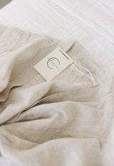 Line Label robe in natural oat colour draped on the bed showing the softness of pure french linen