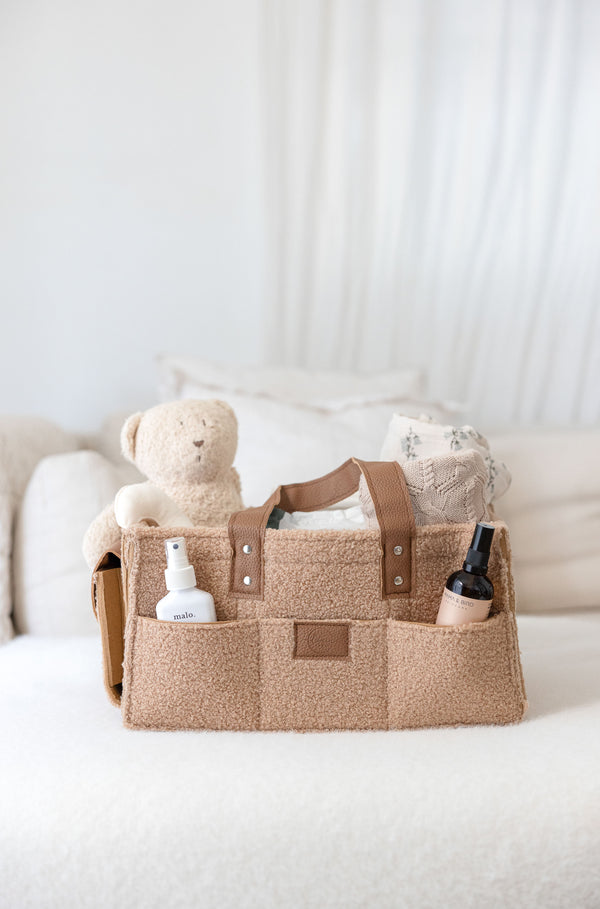 Linen Label Tan colour caddy with textured leather handles and logo. filled with baby products sitting on change table. 