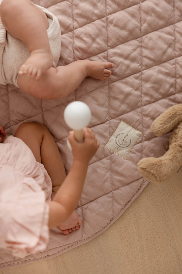 Two babies playing just showing their legs and feet, both on the quilted pure French Linen, Dusty Rose Pink colour featuring the Linen Label logo