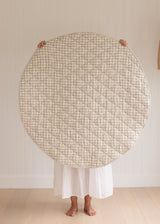 A women holding up a Linen Label Pure French Linen quilted padded play mat folded showing the reverse side of Natural Oat gingham colour side, she hold it over her face and baby to show the size. 