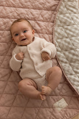A close photo of a baby kicking around and playing on Linen Label Pure French Linen showing the quilted padded detail of the play mat. The edge is folded showing both sides, one side Dusty Rose Pink and the other side is Natural Gingham check