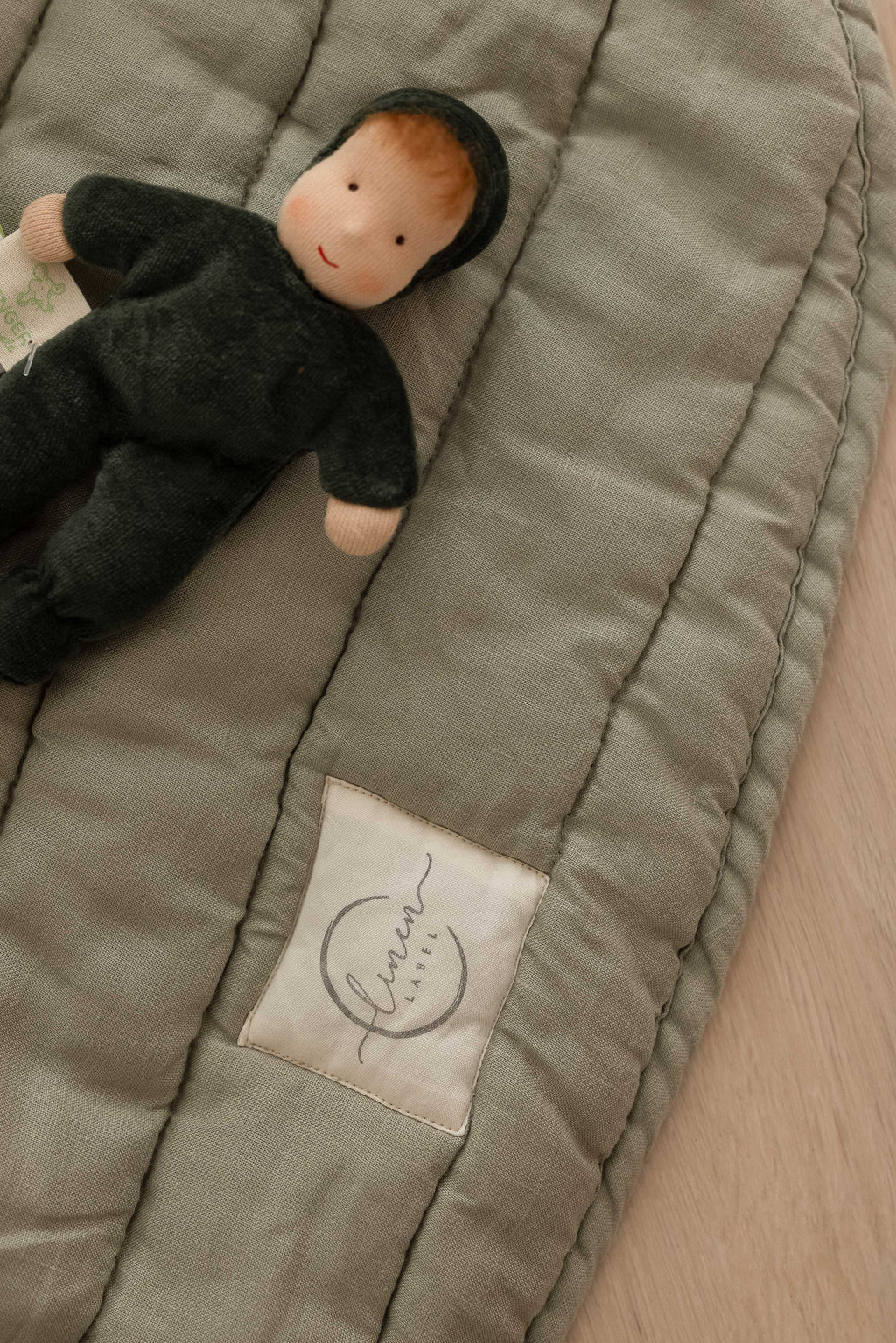 close-up photo on Linen Label logo showing the soft sage green colour as well as a little dolly toy in green