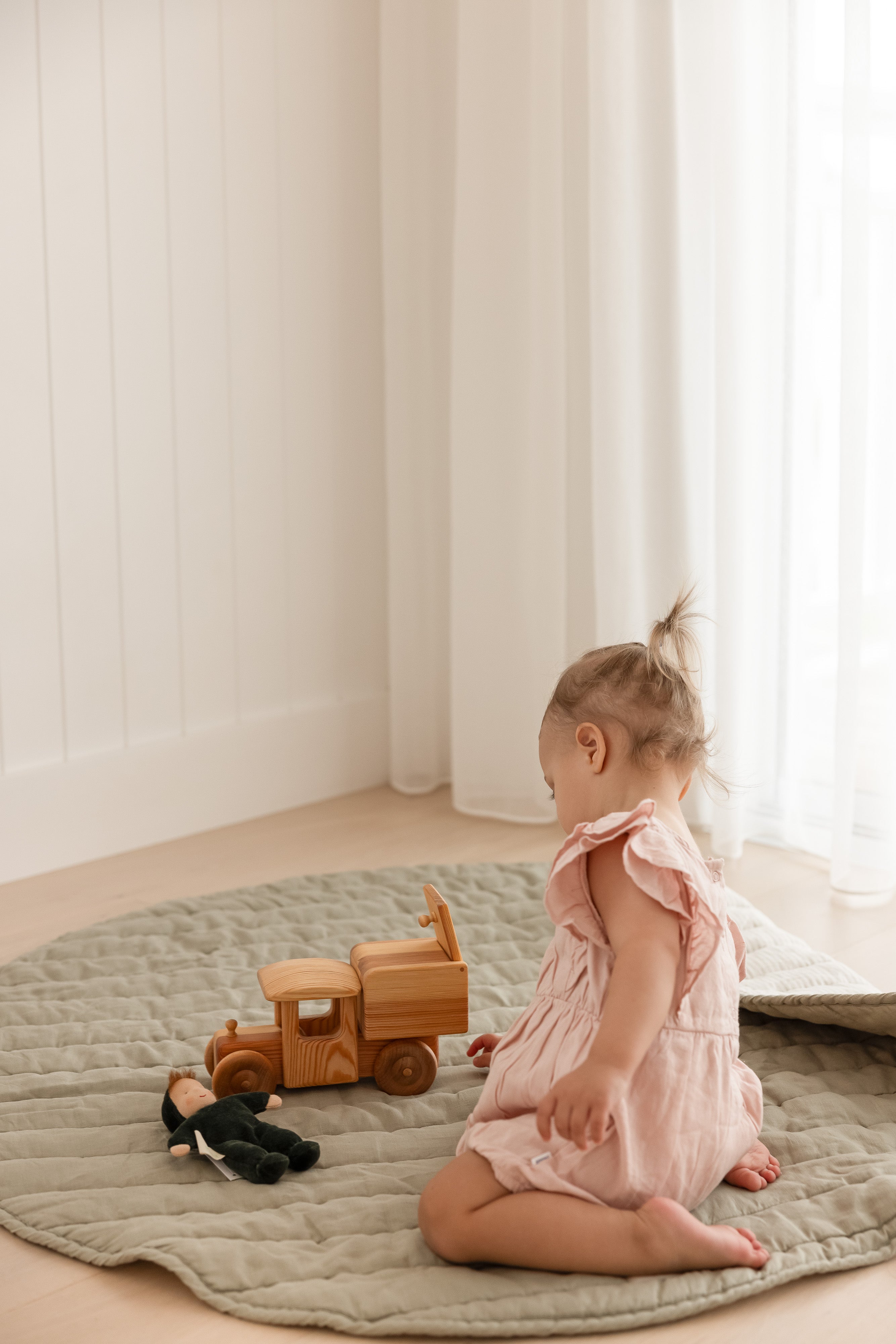 Baby toddler playing with a wooden truck playing on Linen Label Pure French Linen quilted padded play mat. The mat edge is folded showing both sides, one soft sage green colour and the other natural pinstripe colour