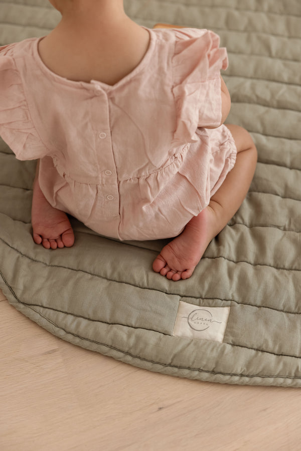 Baby feet and legs playing on Linen Label Pure French Linen quilted padded play mat featuring the Linen Label logo one soft sage green colour 