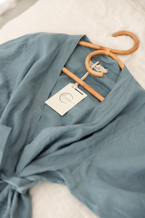 Linen Label Dusty Denim Blue French Linen Bathrobe Kimono Robe draped on the bed on a hanger - looking luxurious and aesthetically pleasing in a Dusty Rose, perfect for ultimate comfort and relaxation. Crafted with 100% French Linen that grows softer with each wash