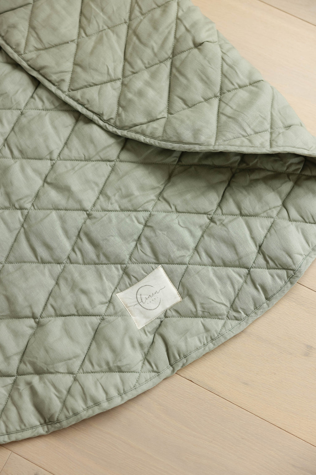 Soft sage play mat on a timber floor with the corner flipped showing the thickness and how plus the play malt is by Linen Label