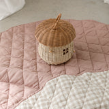 Linen Label Pure French Linen quilted padded play mat folded with cane toy basket. The playmat is showing both sides, one side Dusty Rose Pink colour and the other Gingham check