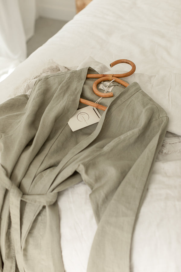 Linen Label Soft Sage Green French Linen Bathrobe Kimono Robe draped on the bed on a hanger - looking luxurious and aesthetically pleasing in a sage green, perfect for ultimate comfort and relaxation. Crafted with 100% French Linen that grows softer with each wash