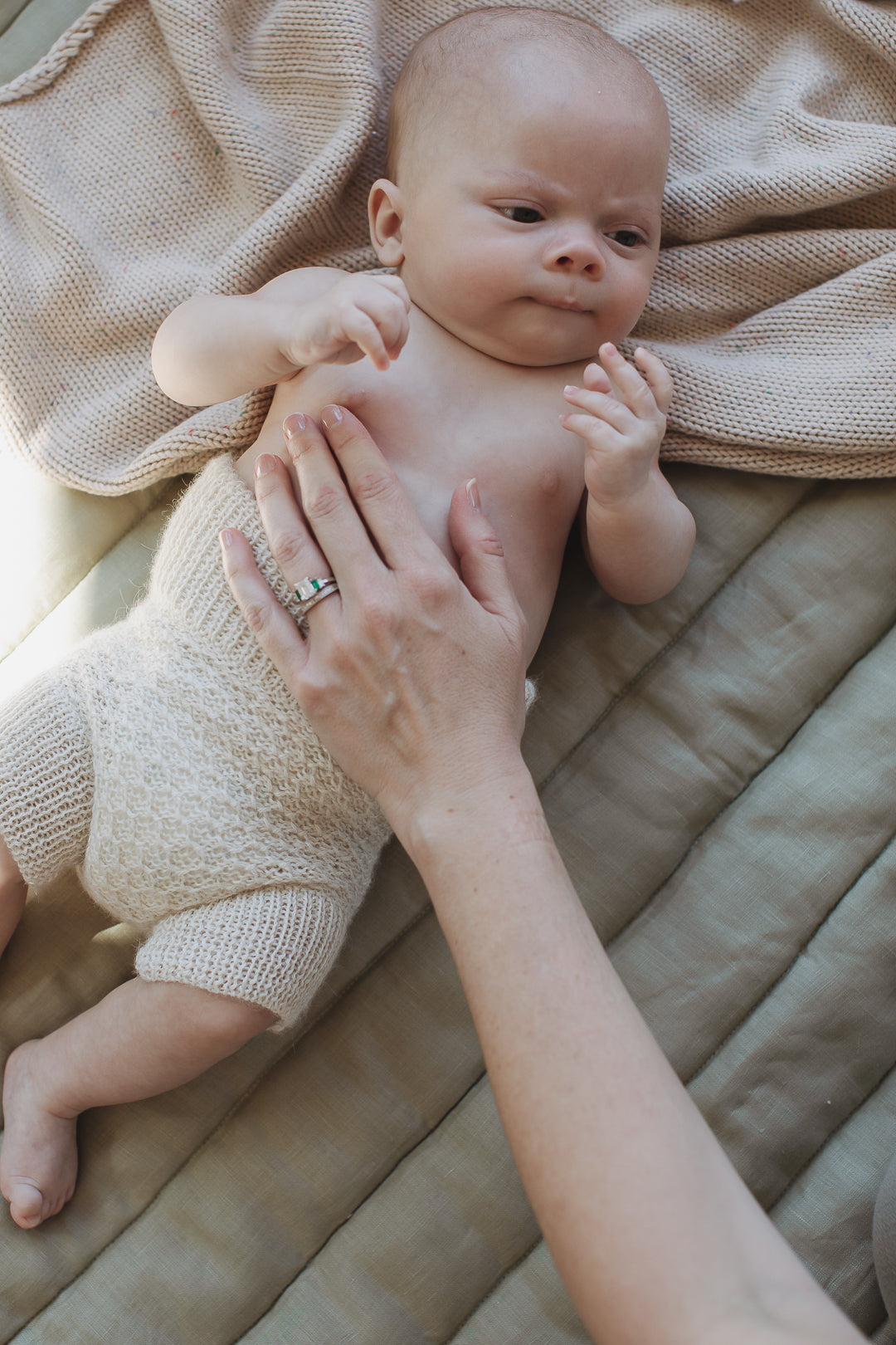 Baby laying on Linen Label soft sage green quilted play mat with a mothers hand gently resting on the baby.st