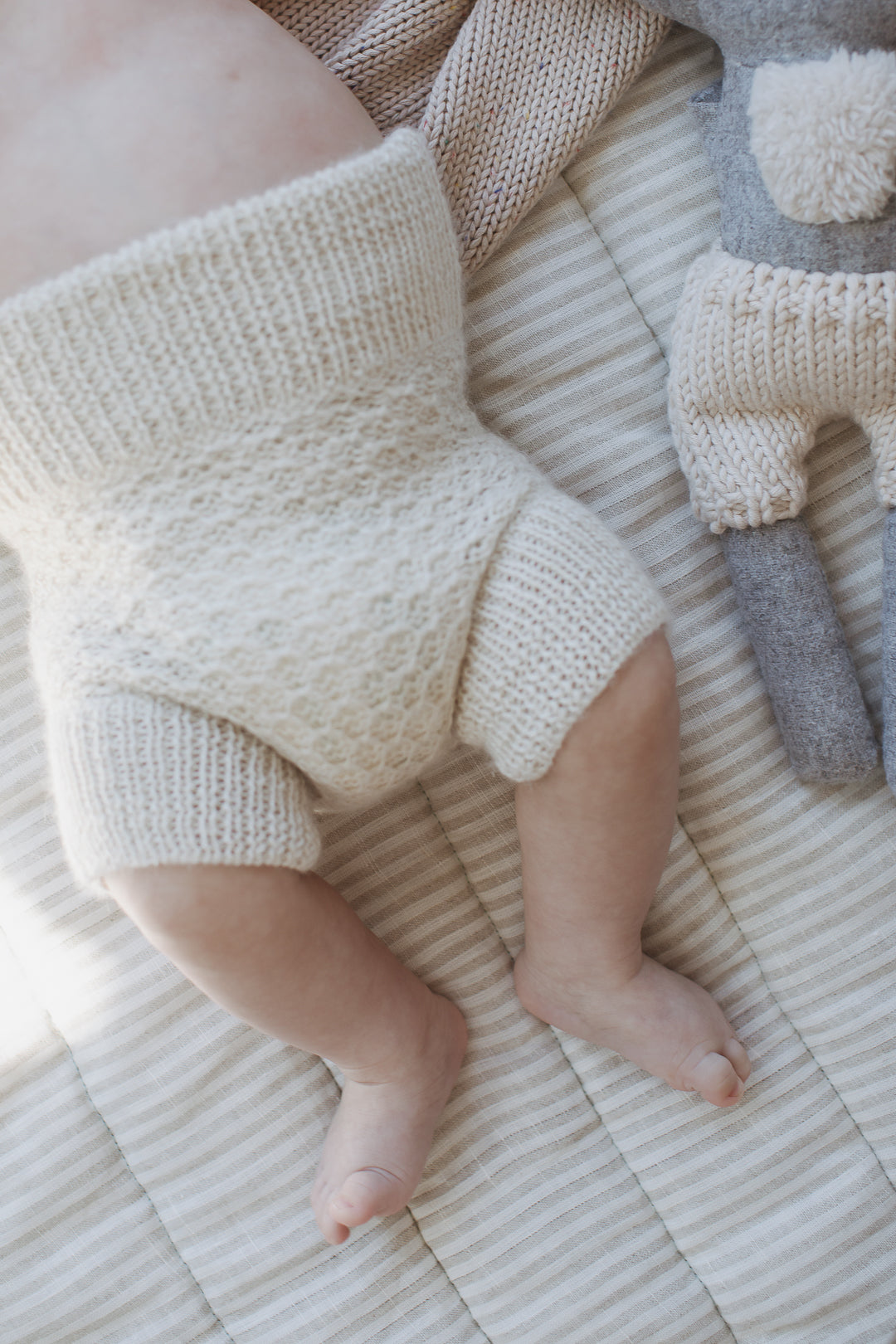Linen label Play mat close newborn baby and teddies legs on the quilted showing the reversible side in natural pinstripe as well as showing the quilting detail and high quality of the mat