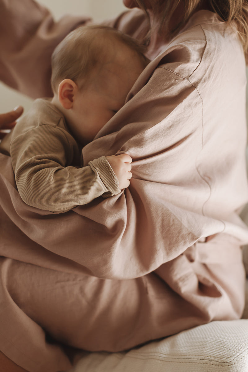 Baby snuggles into mother chest feeling the softness  of the French Linen Robe in Dust Rose Pink robe, Kimono, bathrobe the mother is wearing. 