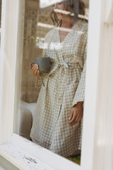 Woman looking out at the morning sun in her Linen Label Natural Oat gingham French Linen Bathrobe Kimono - looking luxurious in her soothing sage green linen robe, perfect for ultimate comfort and relaxation. Crafted with 100% French Linen that grows softer with each wash. Ideal as a dressing gown, bathrobe, or pyjamas