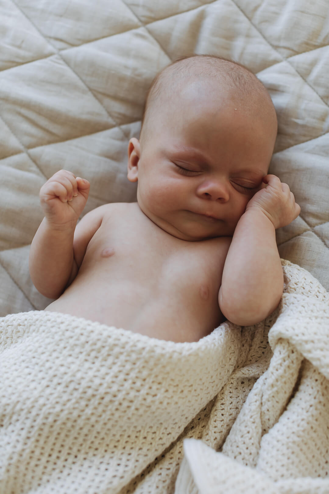 A tiny newborn baby sleeping on the Linen Label pure French Linen quilted padded play mat folded showing the softness of the Natural Oat colour and the other Gingham check